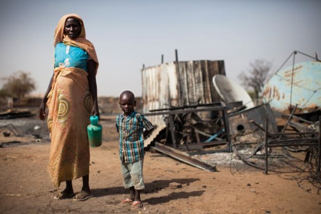 Una madre y su hijo junto a los restos quemados de su casa en Khor Abeche, en el sur de Darfur, en abril de 2014. Crédito: Foto de la ONU / Albert González Farran