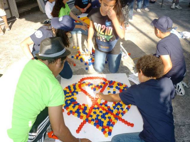 Unos adolescentes crean con tapones el lazo que simboliza la lucha contra el sida, en una de las actividades que se repiten en América Latina para concienciar a la población sobre la enfermedad. Crédito: Onusida América Latina