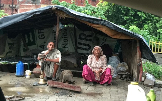 Una pareja de personas mayores sentada frente a su “casa”, una estructura hecha con bolsas de plástico y materiales de desechos. Crédito: Neeta Lal/IPS