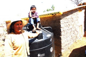Una de las horticultoras periurbanas de las afueras de Sucre junto a su hijo, subido orgulloso en el tanque de agua, donado por la gobernación de Chuquisaca y con capacidad para 2.000 litros, donde almacena el agua de lluvia para luego filtrarla mediante goteo a las verduras orgánicas que ella cultiva. Crédito: Franz Chávez/IPS