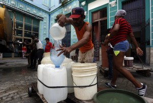 Un hombre llena varios envases con agua potable procedente de un camión cisterna, en una calle de La Habana Vieja, en la capital de Cuba. Las dificultades del abastecimiento del recurso a los hogares, por problemas estructurales en la red de suministro y una aguda sequía, trastoca la vida de los habitantes de La Habana, en especial de las mujeres. Crédito: Jorge Luis Baños/IPS