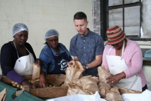 Christopher D'Aiuto, especialista en suelos y coordinador de producción de Harvest of Hope ayuda a un grupo de mujeres de la organización Abalimi Bezekhaya a preparar los paquetes con verduras frescas. Crédito: Astrid Stark/IPS.