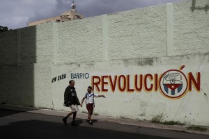 Dos personas transitan al lado de una cartel en el que puede leerse la frase “En cada barrio revolución”, en una calle de Centro Habana, en la capital de Cuba, que resalta la importancia de cada asentamiento para el poder político del país. Crédito: Jorge Luis Baños/IPS