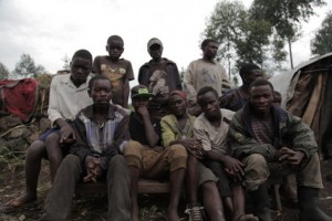Un grupo de jóvenes bambutis de Biganiro, RDC, sentados frente a sus casas, estructuras provisionales hechas de madera y láminas de plástico. Crédito: Zahra Moloo / IPS