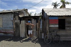 Una mujer ante la entrada de su vivienda, construida sobre la arena del tibaracón de la desembocadura del río Macaguaní, en el municipio de Baracoa, en el oriente de Cuba. Los pobladores de su asentamiento deberán ser reubicados por la vulnerabilidad climática del lugar. Crédito: Jorge Luis Baños/IPS
