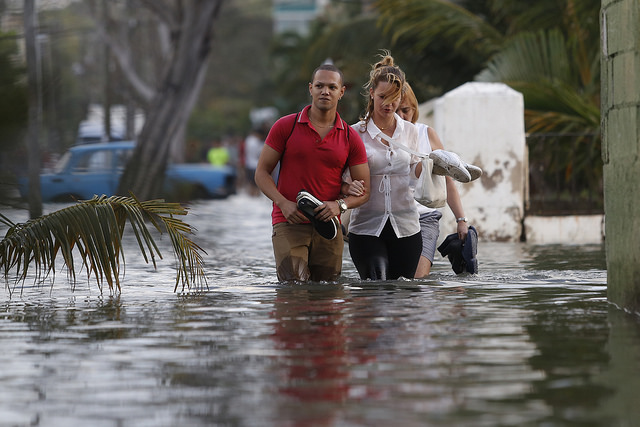 Tres personas transitan con el agua por las rodillas por una céntrica calle inundada en enero de 2017 por la penetración del mar, en el barrio del Vedado, en La Habana, la capital de Cuba, con una creciente vulnerabilidad ante los efectos del cambio climático. Crédito: Jorge Luis Baños/IPS