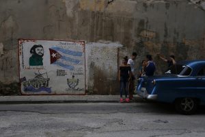 Un grupo de jóvenes cubanos conversa cerca un grafiti donde aparece la imagen del expresidente Fidel Castro y su concepto de Revolución, en el centro de La Habana. Crédito: Jorge Luis Baños/IPS