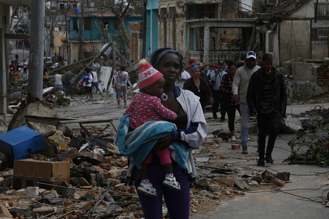 Una mujer camina con un bebe en sus brazos, entre los escombros dejados en el municipio de 10 de Octubre, uno de los que conforman La Habana, después que la capital cubana fuese azotada por un violento tornado la noche del 27 de enero. Crédito: Jorge Luis Baños/IPS