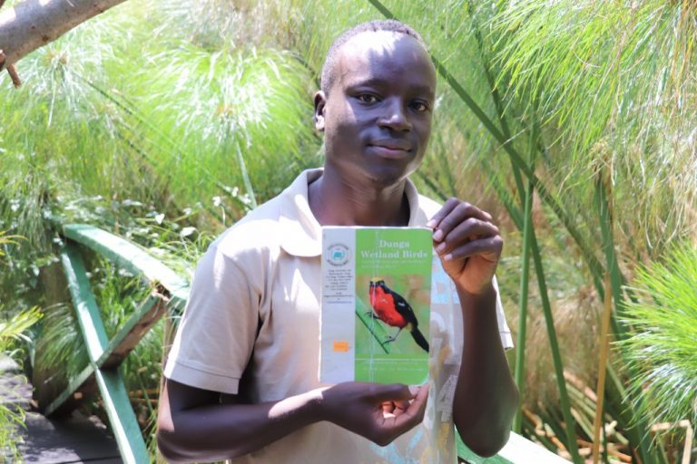 Edgar Ochieng, guía de la pasarela de papiros en la playa de Dunga, sobre el lago Victoria, en Kenia, muestra el manual que un grupo juvenil de ecoturismo han elaborado sobre las aves endémicas del lugar, uno de los atractivos de visitantes extranjeros en este humedal costero del segundo mayor cuerpo de agua dulce del mundo. Foto: Isaiah Esipisu / IPS