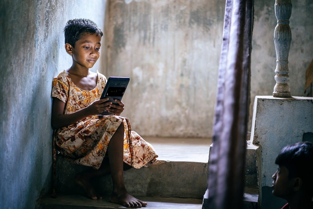 Una niña en un barrio pobre y hacinado de Bhubaneswar, en India, revisa sus tareas de aprendizaje electrónico en una tableta. Foto: Cortesía de John Marshall / Aveti Learning