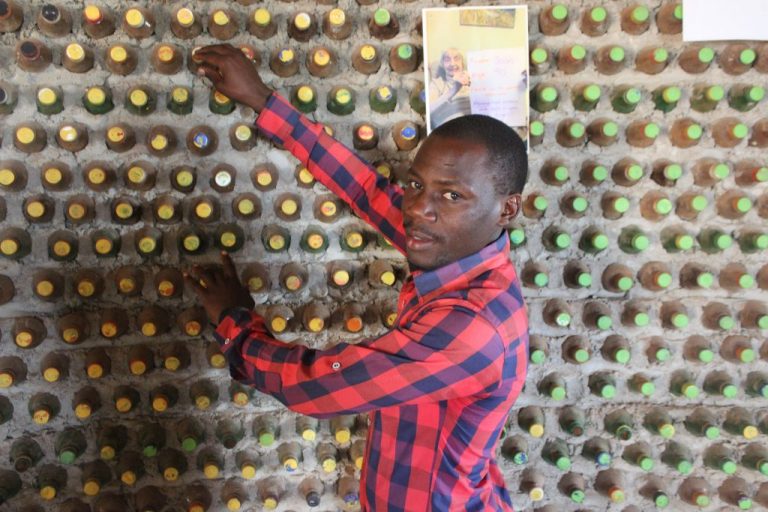 David Mande muestra una pared de una casa construida con ecoladrillos, elaborados con botellas plásticas rescatadas de la basura que se rellenan con tierra húmeda que luego se endurece. Cada botella se cierra herméticamente para que terminen transformándose en paredes firmes y convertirse así en solución sostenible y barata al déficit de vivienda en Uganda. Foto: Wambi Michael / IPS