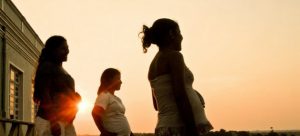 Tres mujeres afectadas por covid en embarazadas viendo al horizonte durante el atardecer.