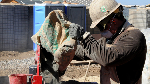Obrero con cubrebocas vertiendo bolsa de cemento en máquina, muestra de uno de los millones de trabajos perdidos.