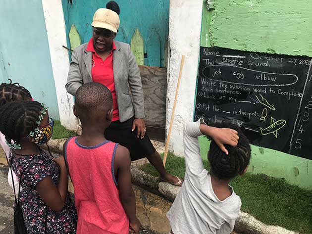 Un grupo de escolares recibe clases de una maestra en una comunidad de bajos recursos de Kingston, la capital de Jamaica. Para ello, la docente improvisó pizarrones en las paredes para que sus alumnos sigan instruyéndose pese al cierre de las escuelas por la pandemia de covid. Foto: Kate Chappell