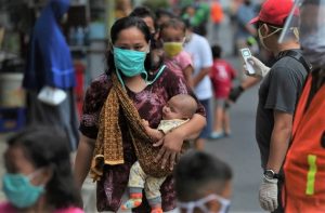Una madre indonesia camina con sus hijos por una calle. Todos menos el bebe que lleva en brazos portan mascarillas, una protección ante la covid que se universalizó en el mundo en 2020. Foto: Achmad/Banco Mundial
