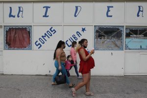 Tres mujeres y una niña transitan, protegidas por sus mascarillas, por una calle de La Habana, junto a un cartel donde se lee: “Somos Cuba”. Pese a ser un país pequeño y con recursos financieros limitados, la industria biofarmacéutica tiene un alto desarrollo en Cuba y representa una importante fuente de ingresos para el Estado. Foto: Jorge Luis Baños/IPS