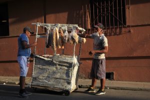 Un vendedor ambulante de panes y galletas atiende a un cliente en su precario puesto en una calle de La Habana, en Cuba. Los confinamientos, el corte de la cadena de suministros y la crisis económica por la pandemia, hundieron los ingresos, sobre todo quienes trabajan en el sector informal, que suelen ser también los más expuestos a la covid, pues no pueden trabajar a distancia o pedir una licencia para proteger su salud. Foto: Jorge Luis Baños/IPS