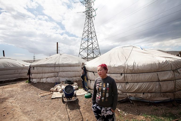 Una mujer fuera de un grupo de yurtas (viviendas móviles de los nómadas) en el distrito de Ger, cerca de la capital mongola, Ulaanbaatar, al lado de la red eléctrica. El gobierno de Mongolia está tomando medidas aceleradas para que en el país domine la energía limpia y que en 2050 se alcance la meta de emisiones netas cero de gases contaminantes. Foto: Nathalie Daoust/ CC BY-SA 4.0