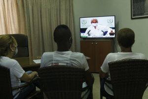 Tres personas observan la transmisión del parte informativo que ofrece el Francisco Durán García, director nacional de Epidemiología del Ministerio de Salud Pública sobre el comportamiento de la covid-19 en Cuba. El sistema de salud pública cubano, universal y gratuito, ha debido gestionar nuevos centros de aislamiento, camas adicionales en las salas de terapia, fármacos para mejorar el estado inmunológico de las personas y ventiladores pulmonares para asistir a las y los pacientes críticos, entre otros insumos. Foto: Jorge Luis Baños/IPS