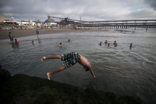 Residentes de Quintero y Puchuncaví se bañan en la playa de Ventanas, con el parque industrial de fondo. Foto: Diego Figueroa
