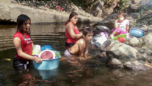 Una madre lava platos y otros objetos de cocina mientras sus hijos se recrean por un rato en un río en la zona rural de El Salvador, donde la falta de agua lleva a muchas familia a proveerse del recurso en lagos y ríos. En algunos lugares, los productores de caña han desviado esos afluentes para regar sus cultivos, algo que en principio va a ser regulado con la nueva Ley de Recursos Hídricos, aprobada el 21 de diciembre. Crédito: Edgardo Ayala / IPS