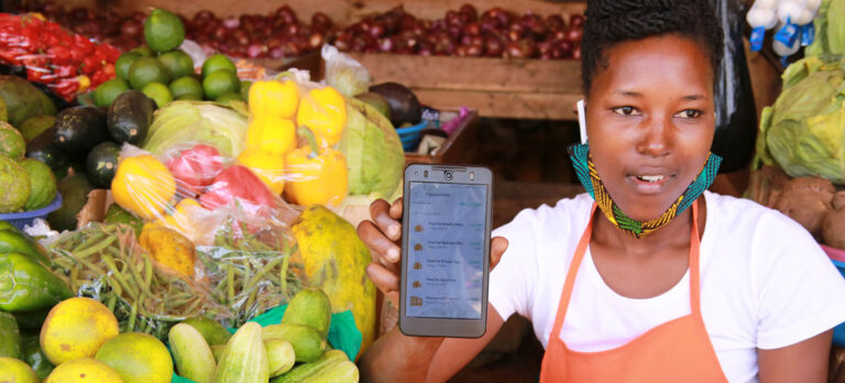 Una vendedora en un mercado de Kampala, Uganda, utiliza la aplicación SafeBoda para conectarse con sus clientes durante los bloqueos por la covid-19. Esa enfermedad es uno de los cuatro factores que merma el crecimiento económico previsto para 2022, en comparación con el año pasado. Foto: FNUDC